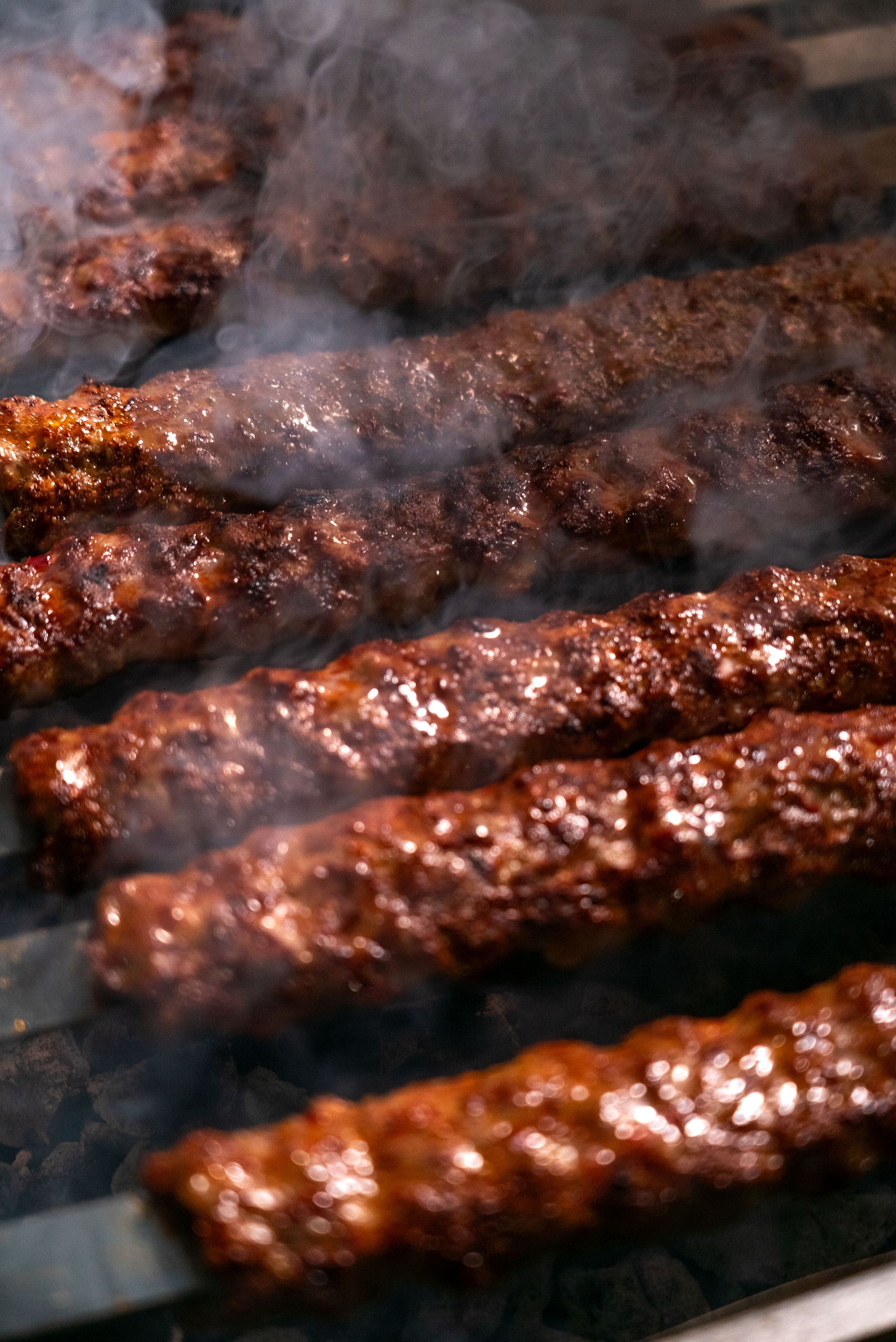 Close-up of grilled kebabs sizzling on a barbecue with smoke, showcasing deliciously cooked meat.